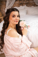 A beautiful bride poses gracefully by a sunlit window, wearing a delicate lace robe. The light highlights her serene expression and the intricate details of her bridal attire