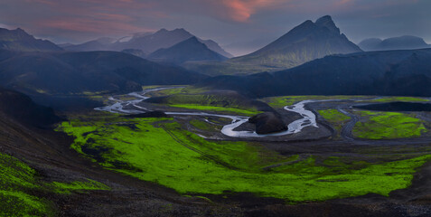 Serpentine glacial rivers weave through neon green moss and dark lava in Iceland's Landmannalaugar...