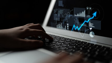 A close-up view of a person hands typing on a laptop keyboard while analyzing data with graphic...