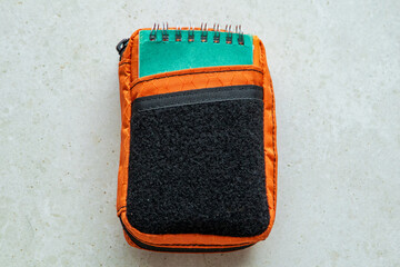 Compact orange tactical pouch with black velcro panel and small spiral notebook. EDC gear organizer