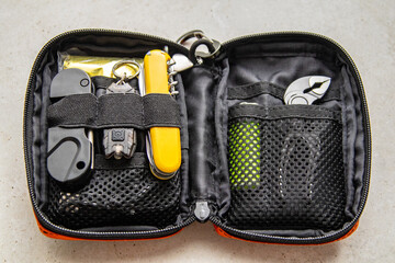 Open orange EDC pouch with multitool, flashlight, lighter, and other survival gear. Everyday carry organizer