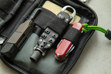 Closeup of EDC pouch with multitool, folding knife, flashlight and tactical screwdriver. Everyday carry setup