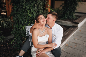 Fototapeta premium Wedding photography, portrait of happy smiling newlyweds, stylish groom and beautiful young brunette bride, hugging outdoors on the street in the city, in the park.