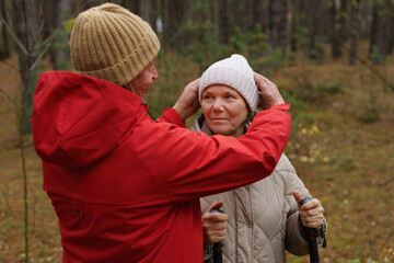 Fototapeta premium A couple shares a tender moment in a forest, adjusting each other's hats while enjoying a hike during the colorful autumn season