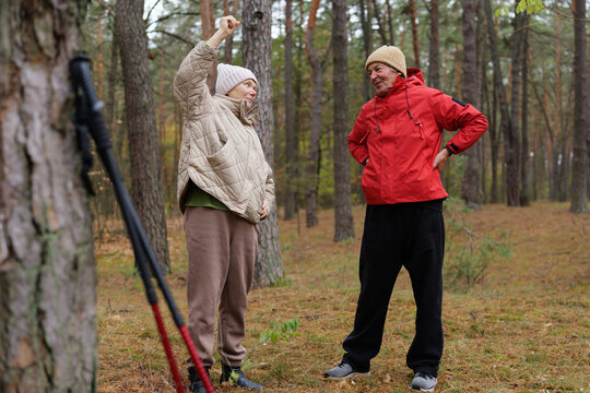 A couple stands in a scenic forest, sharing a thoughtful conversation. They are dressed warmly, enjoying the serene surroundings of nature in autumn