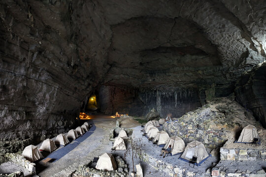Aerial view of tents nestled within the cavernous Ditang Caves, illuminated by soft light, creating a stark contrast against the dark, textured rock formations, Ditang Caves, Guizhou, China.