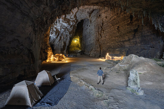 Aerial view of Ditang Caves, where tents nestle in the cavernous space, illuminated by soft light, contrasting with the rugged rock formations, Ditang Caves, Guizhou, China.
