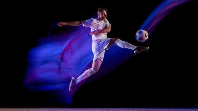 Soccer player jumping and kicking ball with abstract color trail. Concept of creativity in sports visuals, motion energy, and modern advertising for fitness and athletics brands.