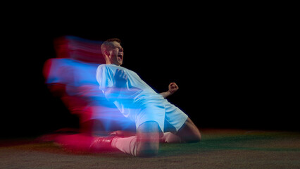 Soccer player celebrating goal on knees with red and blue motion streaks. Concept of passion,...