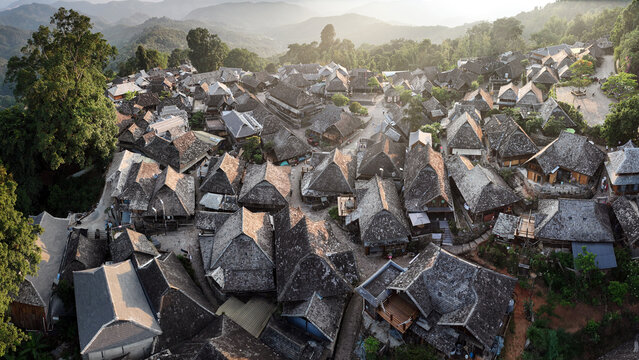 Aerial view of traditional houses nestled amidst verdant hills, a tapestry of earthy tones and textures under the soft glow of the sun, Wengji, China.