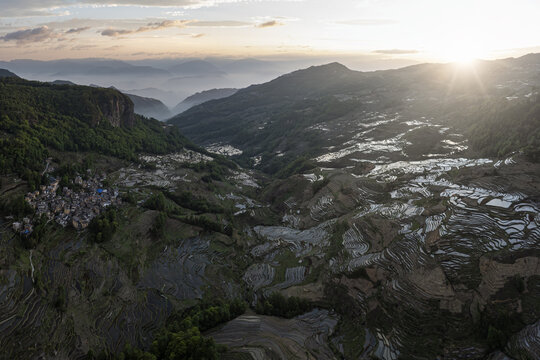 Aerial view of the terraced rice paddies cascading down the mountainside, reflecting the golden light of the setting sun, Honghe Hani and Yi Autonomous Prefecture, Yunnan, China.