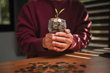 A person holding a glass jar filled with coins and a small green plant growing on top, symbolizing financial growth, savings, and investment for a sustainable and prosperous future.
