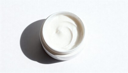 Close-up shot of a white cream in a jar, with a shadow on a white surface.
