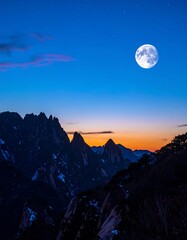 Majestic mountain peaks silhouetted against a twilight sky with a full moon