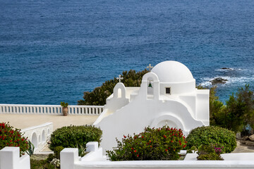 scenic view of aegean sea coast with greek whitewashed chapel surrounded by greenery. church on the deep blue sea backdrop