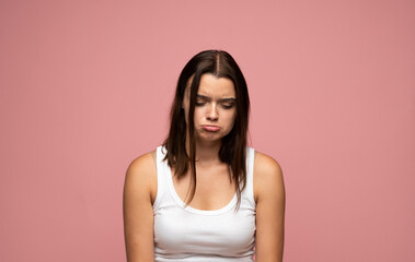 Obraz premium Sad emotion of young woman looking down with pouting lips on pink background