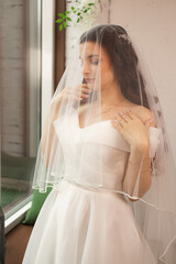 Closeup shot of elegant, brunette bride in vintage white dress posing under veil closeup. Bride portrait wedding makeup and hairstyle, fashion bride. Beautiful bride in veil.
