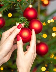 Woman decorates Christmas tree with red ornaments in warm light.