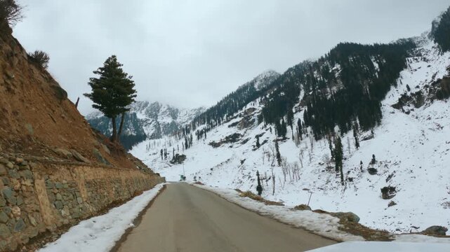 4K POV shot of a vehicle driving through a narrow asphalt road on the side of the Himalayan mountains covered by snow in winter season towards Chandanwari from Pahalgam in Jammu and Kashmir, India.	
