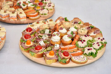 Variety of canapés - small and decorative finger food served on a round wooden plate