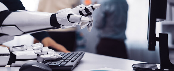 A close-up shot of a robotic arm interacting with a computer keyboard, showcasing modern technology in a business environment, with professionals collaborating in the background.Noogenesis