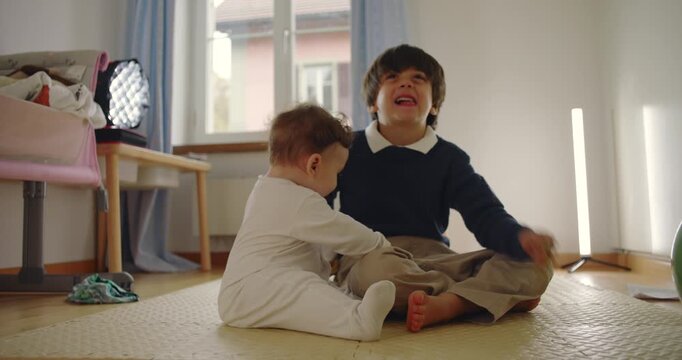 Baby pulling older brother&rsquo;s hair while playing together on floor, unaware of causing discomfort in innocent sibling interaction at home
