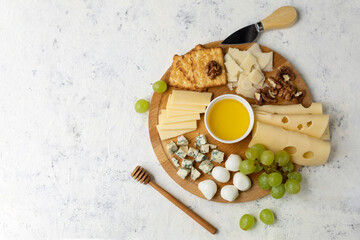 Assorted cheese platter with grapes, honey, and crackers on wooden board