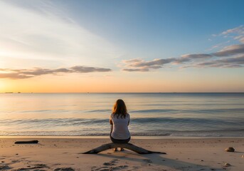 Solitary person sitting on a sandy beach facing a calm ocean during sunrise with wide horizon