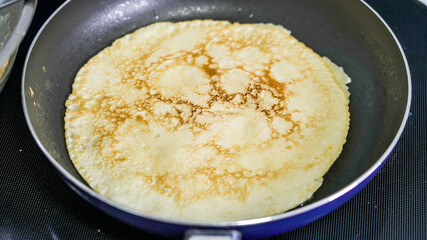 Crepe cooking on a non-stick pan with a golden brown color and a smooth texture