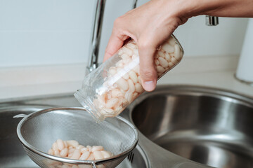 man pours cooked white beans into a metal strainer