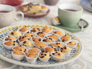 Mini chocolate cupcakes on patterned ceramic plate. Holidays and lifestyle. Food on table covered with tablecloth. 