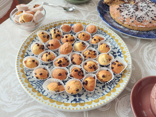 Mini chocolate cupcakes on patterned ceramic plate. Holidays and lifestyle. Food on table covered with tablecloth. 