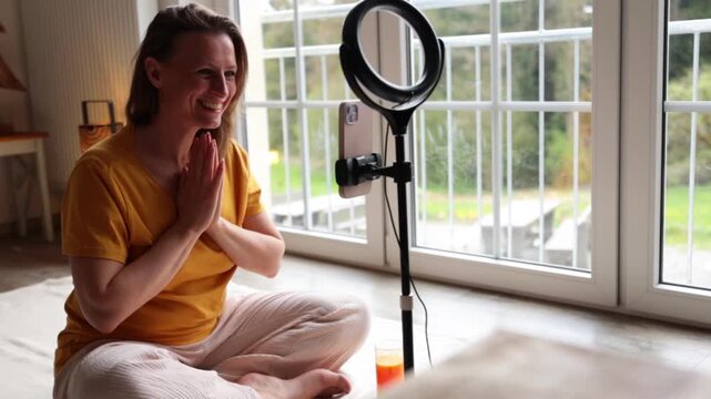 Woman practicing kundalini yoga and teaching an online class from home sitting in lotus position in front of camera during meditation session promoting balance and mental health