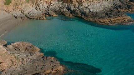 Breathtaking aerial view of a secluded turquoise bay with sandy beach and surrounding rugged coastal rocks