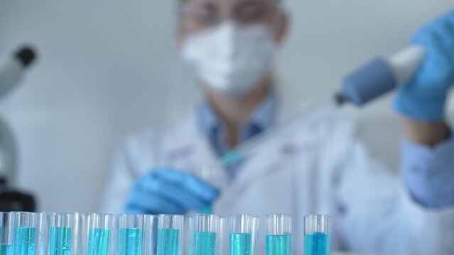 Laboratory tubes are in focus, closeup view. Female scientist researcher is using a micropipette at the lab background. Medicine and science