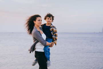 Against a breezy seaside backdrop, a woman carries a child, their expressions a blend of focus and contentment.