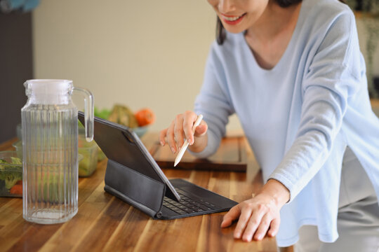 Cropped shot smiling woman using tablet to follow online recipe while preparing healthy food in cozy kitchen, showing lifestyle balance