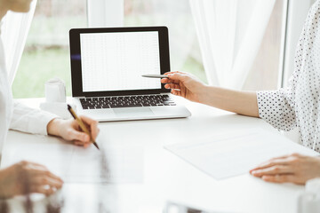Two accountants using a laptop computer for counting taxes at white desk in office. Business Woman pointing into screen with a pen. Teamwork in business audit and finance