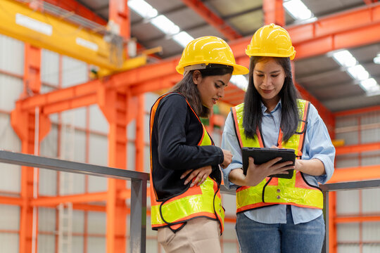 female engineer supervisor discuss with technician foreman use digital tablet to check production plan and timeline, team of diverse workers working together at industrial manufacturing factory