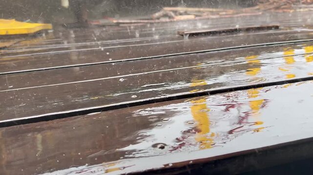 Raindrops falling on a dark, wet surface with reflections of yellow objects.
