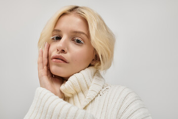 Captivating young blonde woman in cozy knitted sweater stuns in studio setting
