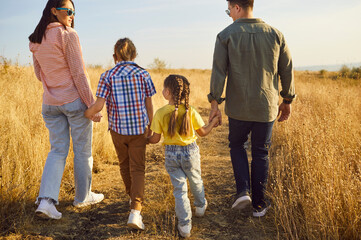 Happy family walking at sunset through meadow togetherness. In warm nature summer light, parents...