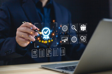 Businessman using digital pen with hologram quality assurance certification icon and five stars rating on laptop screen, concept of standard approval, customer satisfaction, and business excellence.