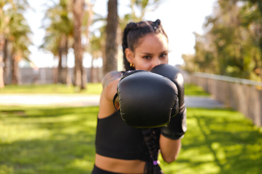 confident Hispanic woman training boxing outdoors wearing gloves