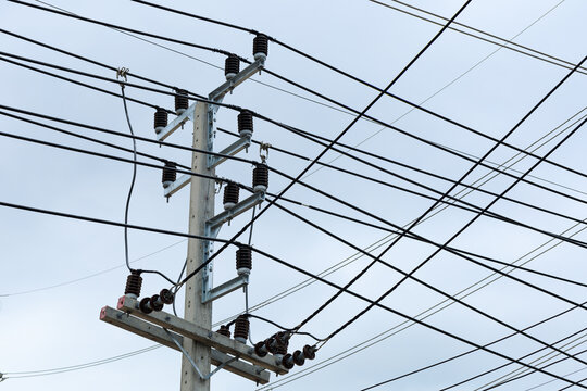 This image captures a chaotic tangle of black electric wires and communication cables overloading a concrete utility pole, symbolizing urban complexity and aging infrastructure.