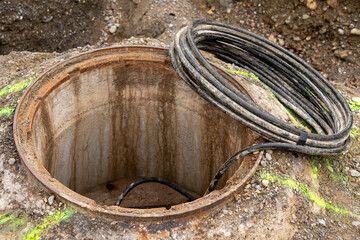 Open man hole with a role of black cable on the ground, leading into the man hole. Dug out earth around.