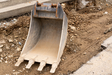 Excavator bucket on the ground, on the earth where the street has been jpartly removed, between curb and rest of the street.