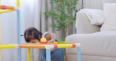 Asian toddler girl standing near sofa playing with colorful toys, exploring balance and coordination, concept of slowmotion child development, curiosity, and early learning in cozy home - Powered by Adobe