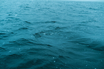 Deep blue ocean water surface with gentle waves and falling snow during overcast weather