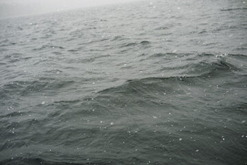 Dark gray water surface with small waves and falling snow flakes
